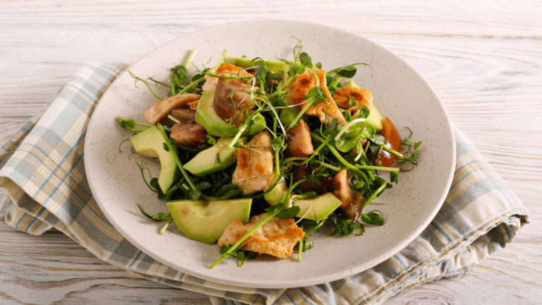 Plate of pea-shoot microgreens salad with avocado slices, browned meat strips and mushrooms on a checked cloth