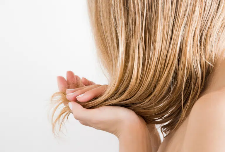 Close-up from behind of a woman's long, glossy blonde hair as she cradles the ends in her open hand against a plain white background