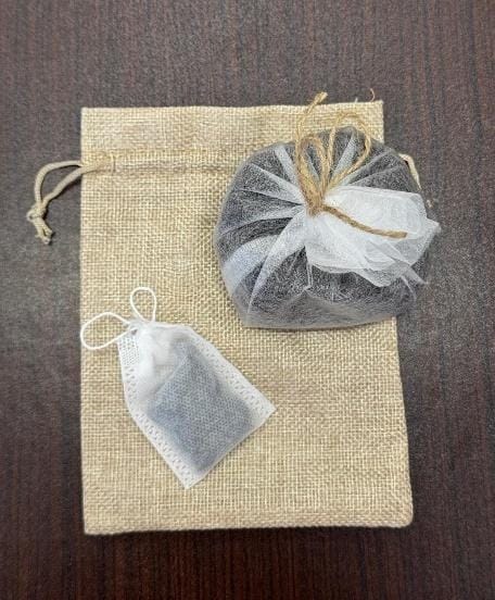Beige jute drawstring bag on a wooden table with two mesh pouches of dark seeds resting on top of it