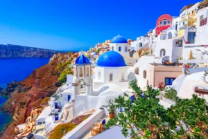 Whitewashed Greek island houses and blue-domed churches stacked on a caldera cliff above deep blue sea under a clear sky