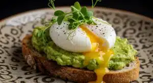 Toasted sourdough topped with mashed avocado and a poached egg split open with yolk running out, cracked pepper and pea shoots